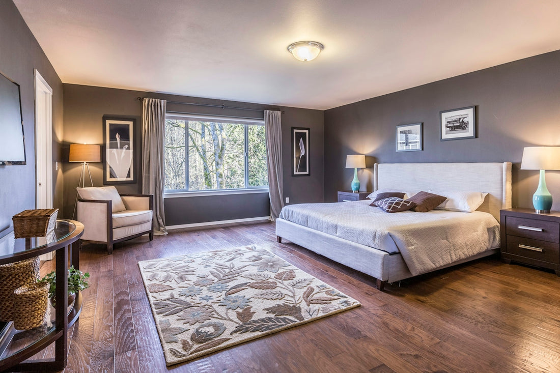 A bedroom with dark grey walls, a large bed, and a floral area rug
